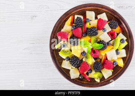 delicious fruit  and berry summer salad decorated with mint leaves on clay dish on white worktop, view from above Stock Photo