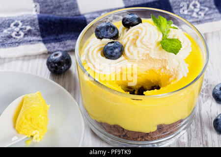 Layered healthy breakfast - Lemon Blueberry cheesecake in glass cup decorated with ice cream, lemon slices and mint. spoon with mousse on saucer, view Stock Photo