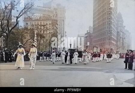 Black and white photograph showing several women, wearing white Edwardian clothing, and sashes, and holding a US flag and pennants, followed by a marching band, taking part in a suffrage parade in New York City, 1913. Note: Image has been digitally colorized using a modern process. Colors may not be period-accurate. () Stock Photo