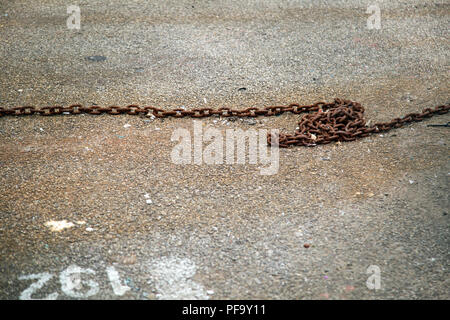 A single rusty chain on a concrete ground Stock Photo