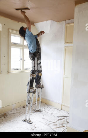 Buckingham, UK - May 07, 2015. A plasterer skims a high ceiling whilst standing on stilts. Stock Photo