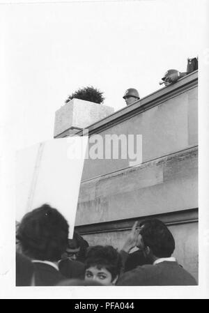 Black and white photograph, showing two helmeted National Guardsmen observing from the vantage point of a raised balcony, with a crowd of people gathered below, including a short-haired brunette woman who looks back but away from the camera, during a march to protest the Vietnam War, photographed in Washington DC, United States, 1969. () Stock Photo