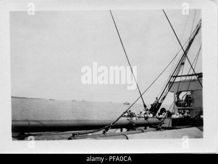 Black and white photograph, with rigging visible in the foreground, showing a group of passengers standing on the deck of a ship that is likely navigating the Gatun Lake section of the Panama Canal, 1915. () Stock Photo