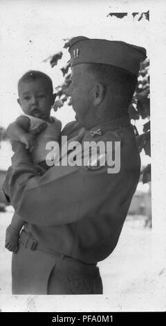 Black and white photograph, showing a male soldier, in profile, from the waist up, wearing a uniform and hat, and holding a baby who faces the camera, likely photographed in Ohio in the during World War II, 1950. ()