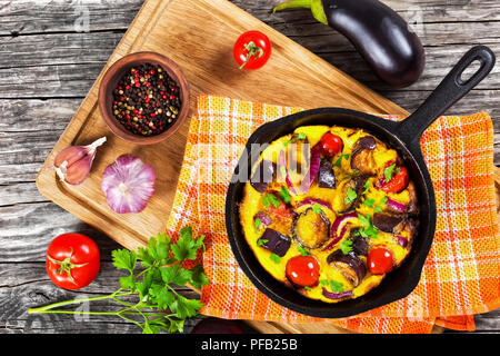 Single Serve Paleo Breakfast Skillet - scrambled eggs and vegetables on kitchen towel on cutting board with pepper in clay bowl, garlic and ripe tomat Stock Photo