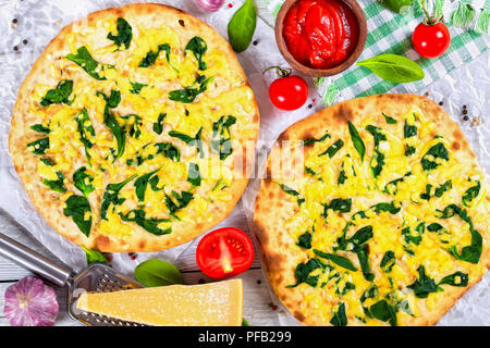 Vegetarian pizza with spinach leaves, parmesan cheese. tomatoes and homemade salsa in bowl, pepper, garlic and grater with piece of parmesan cheese on Stock Photo