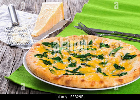 spinach cheese pie on white dish, piece of parmesan cheese and grater on wooden boards, view from above, close-up Stock Photo