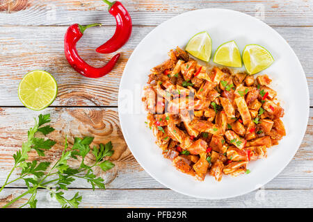 Braised Pig Ears or Oreja de Cerdo with spices, chili pepper, pieces of lime sprinkled with parsley on white platter on natural wooden old boards, top Stock Photo