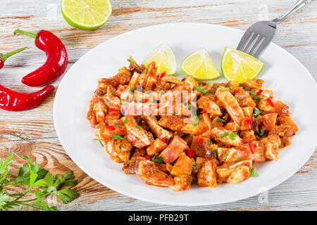 Braised Pig Ears or Oreja de Cerdo with spices,  chilli peppe, pices of lime sprinkled with parsley on white platter on natural wooden old boards, clo Stock Photo