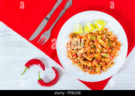 Marinated Pig Ears with spices, chili pepper, pieces of lime sprinkled with parsley on white platte ron red table met,chilli pepper on wooden old boar Stock Photo