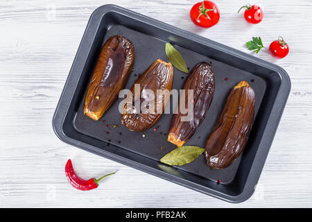 oven baked eggplants in baking dish with bay leaves and spices on white table, view from above Stock Photo