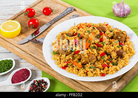 paella with meat, pepper, vegetables and spices on platter on cutting board, lemon slice, spices and cherry tomatoes on background, view from above, c Stock Photo