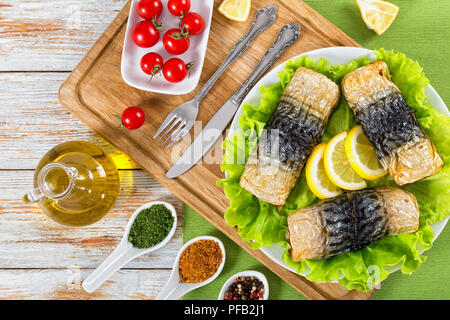 baked fillet of mackerel on lettuce leaves and lemon slices . bottle with olive oil and ceramic spoons with spices on white peeling paint boards, view Stock Photo