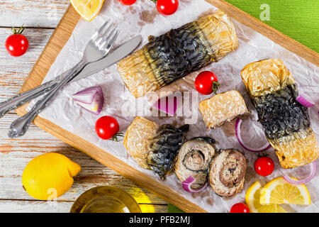 healthy baked fillet of mackerel in rolls, tomatoes and lemon slices on white parchment paper on cutting board with fork and knife,onion, tomatoes and Stock Photo