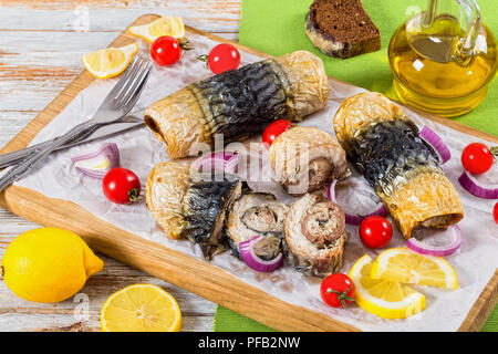 healthy baked fillet of mackerel in rolls, tomatoes and lemon slices on white parchment paper on cutting board with fork and knife,onion and bottle of Stock Photo