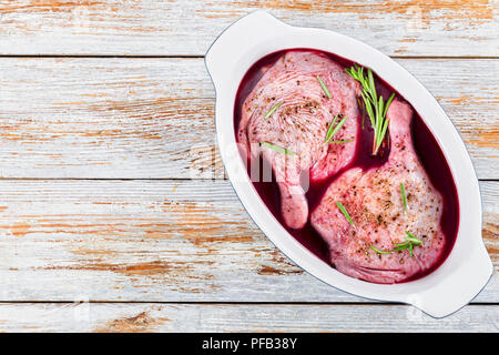 raw duck legs preparing for roasting marinated in red wine with spices, rosemary  on ceramic roasting dish on white planks, copy space left,  view fro Stock Photo