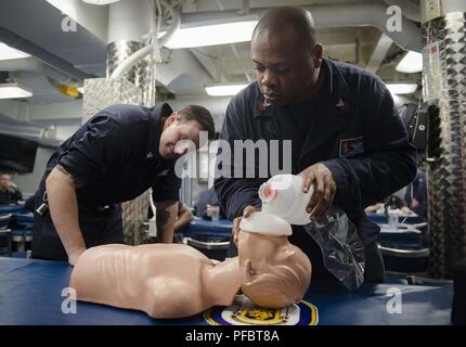 PHILIPPINE SEA (May 31, 2018) Information Systems Technician 1st Class Rickey Parker, right, from Carlyle, Illinois, performs cardiopulmonary resuscitation (CPR) on a training dummy while Logistics Specialist 2nd Class Zachary Mindick, from Prince Georges County, Maryland, observes during a CPR class aboard the Arleigh Burke-class guided-missile destroyer USS Benfold (DDG 65). Benfold is forward-deployed to the U.S. 7th Fleet area of operations in support of security and stability in the Indo-Pacific region. Stock Photo