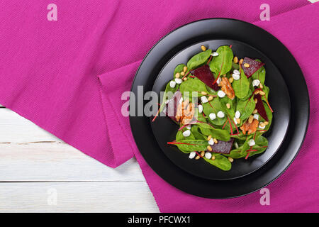 fresh delicious healthy dietary salad of chard leaves, granulated cottage cheese, baked beetroot slices and caramelized walnuts and pine nuts on black Stock Photo