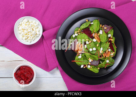 fresh delicious healthy dietary salad of chard leaves, granulated cottage cheese, baked beetroot slices and nuts on black platters, with cranberry sau Stock Photo