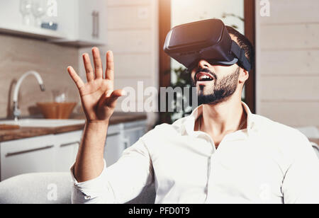 Multicultural bearded man getting experience using VR-headset glasses of virtual reality much gesticulating hands on the modern flat background Stock Photo