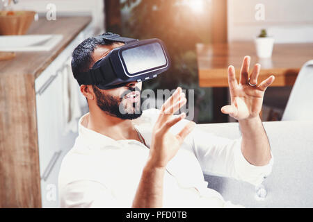 Happy multicultural bearded man getting experience using VR-headset glasses of virtual reality at home Stock Photo