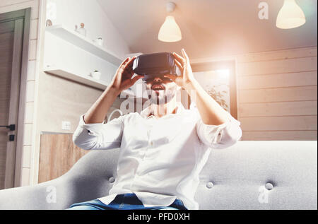Multicultural bearded man laying on the sofa and using virtual reality goggles in the modern flat Stock Photo