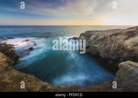 Stunning long-exposure view of smooth waves crashing into rock formations at sunset, Sequit Point, Leo Carrillo State Beach, Malibu, California Stock Photo