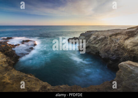 Stunning long-exposure view of smooth waves crashing into rock formations at sunset, Sequit Point, Leo Carrillo State Beach, Malibu, California Stock Photo