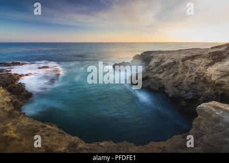 Stunning long-exposure view of smooth waves crashing into rock formations at sunset, Sequit Point, Leo Carrillo State Beach, Malibu, California Stock Photo