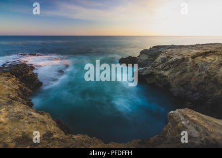 Stunning long-exposure view of smooth waves crashing into rock formations at sunset, Sequit Point, Leo Carrillo State Beach, Malibu, California Stock Photo