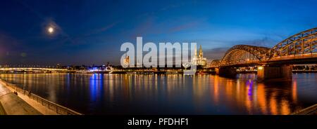 Wide Panorama of Cologne, Germany featuring Cathedral and bridge after sunset at blue hour panorama with river rhine in the foreground Stock Photo