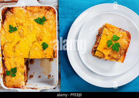 portion of delicious moussaka decorated with parsley cooked for authentic recipe, on plates and in gratin dish on table mat, on white peeling paint  b Stock Photo