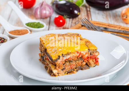 portion of delicious moussaka decorated with parsley cooked for authentic recipe, on plates, on white peeling paint  boards Stock Photo