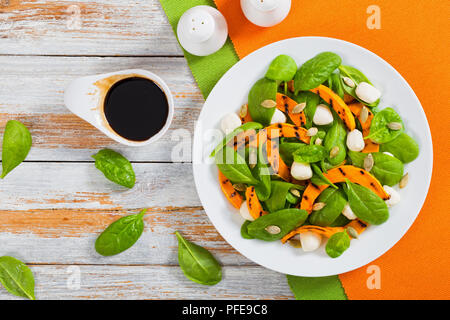 Chargrilled pumpkin, mini mozzarella and spinach salad on white plate with caramelized balsamic vinegar in gravy boat, salt and pepper shakers, view f Stock Photo