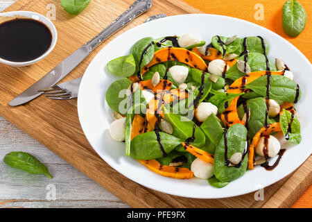 Chargrilled pumpkin, mini mozzarella and spinach salad seasoned with pumpkin seeds on white plate with caramelized balsamic vinegar in gravy boat on c Stock Photo