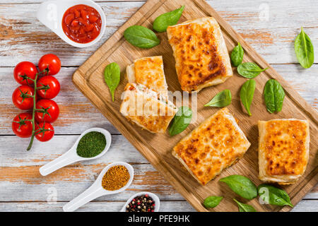 fried Pita or flatbread Stuffed with chicken meat, Cucumber, coleslaw, spinach, dill and sauce on chopping board with ketchup, tomatoes on branch and  Stock Photo