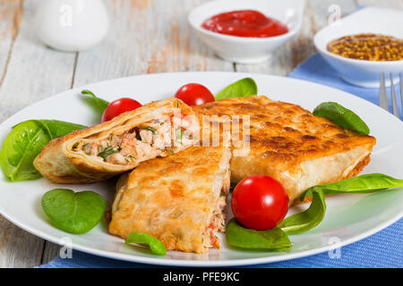 roasted flatbread wraps Stuffed with chicken meat cut in half on white dish with fresh spinach leaves and tomatoes, salt and pepper shakers, ketchup a Stock Photo