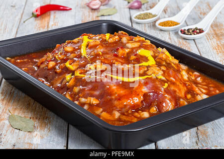 raw meat prepared  to make Texas-style barbequed pork, marinated in barbecue sauce with mustard, fresh onion, dry herbs and spices in roasting dish on Stock Photo