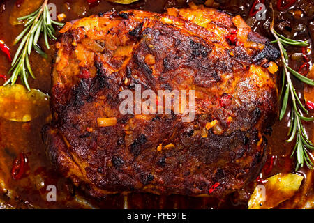 Whole roast shoulder of pulled pork in roasting pan with rich spicy hot marinade and rosemary, authentic texas recipe, view from above, close-up Stock Photo