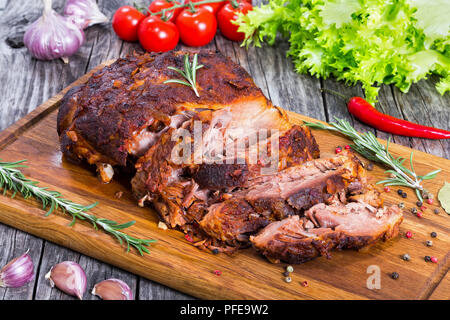 Big Piece of Slow Cooked Oven-Barbecued Pulled Pork shoulder on chopping board with mixed peppercorns, rosemary and garlic, tomato and lettuce salad o Stock Photo