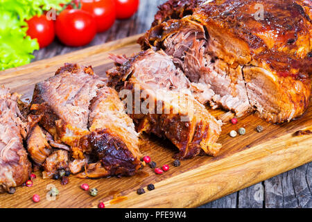 Big Piece of Slow Cooked Oven-Barbecued Pulled Pork shoulder on chopping board with mixed peppercorns, rosemary and garlic, tomato, chili and fresh le Stock Photo