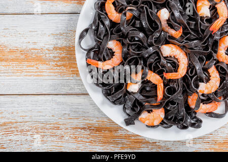 delicious Cuttlefish ink pasta with prawns on white dish on old peeling paint wooden planks, close-up Stock Photo