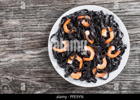 delicious Cuttlefish ink black noodles with prawns on white dish on dark wwoden table, view from above. Stock Photo