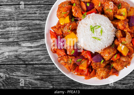 rice with Sweet and Sour fried pork chunks with vegetables, sprinkled with green onion on white dish on dark wooden background, traditional Chinese re Stock Photo