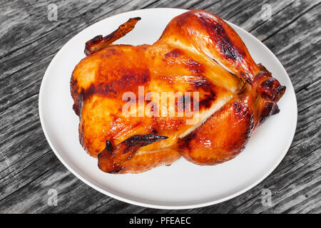 tasty golden crispy skin whole chicken roasted in oven on white platter on old wooden dark table,view from above, close-up Stock Photo