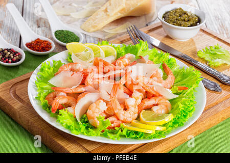 prawns, green lettuce leaves, slices of parmesan cheese salad on white plate with vintage fork and knife. Piece of parmesan, spices and sauce pesto on Stock Photo