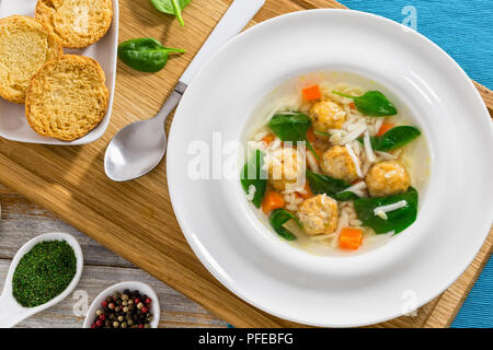 delicious wedding soup with meatball, risini pasta, carrots and spinach in white wide rim bowl with spoon on chopping board,  toasted bread crostini a Stock Photo