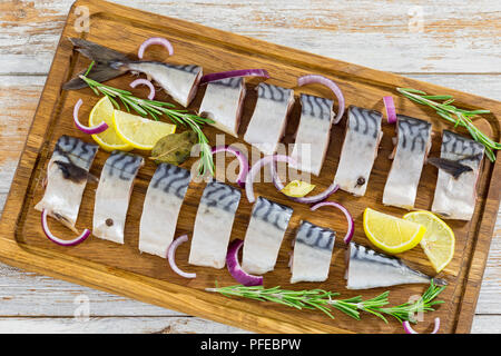 marinated Fillets of Fresh atlantic mackerel fish cut in slices on chopping board with rosemary, lemon, red onion and spices, close-up Stock Photo
