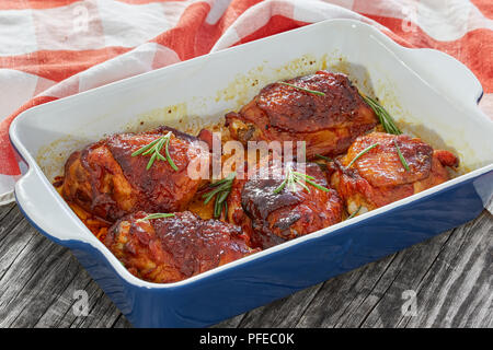 grilled chicken thighs marinated with rosemary and spices in rectangular roasting dish with kitchen towel on old white wooden boards,  view from above Stock Photo
