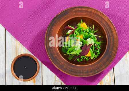 persimmon, blue cheese, spinach, arugula, lettuce leaves and walnuts delicious salad in clay plate with balsamic vinegar dressing on wooden background Stock Photo